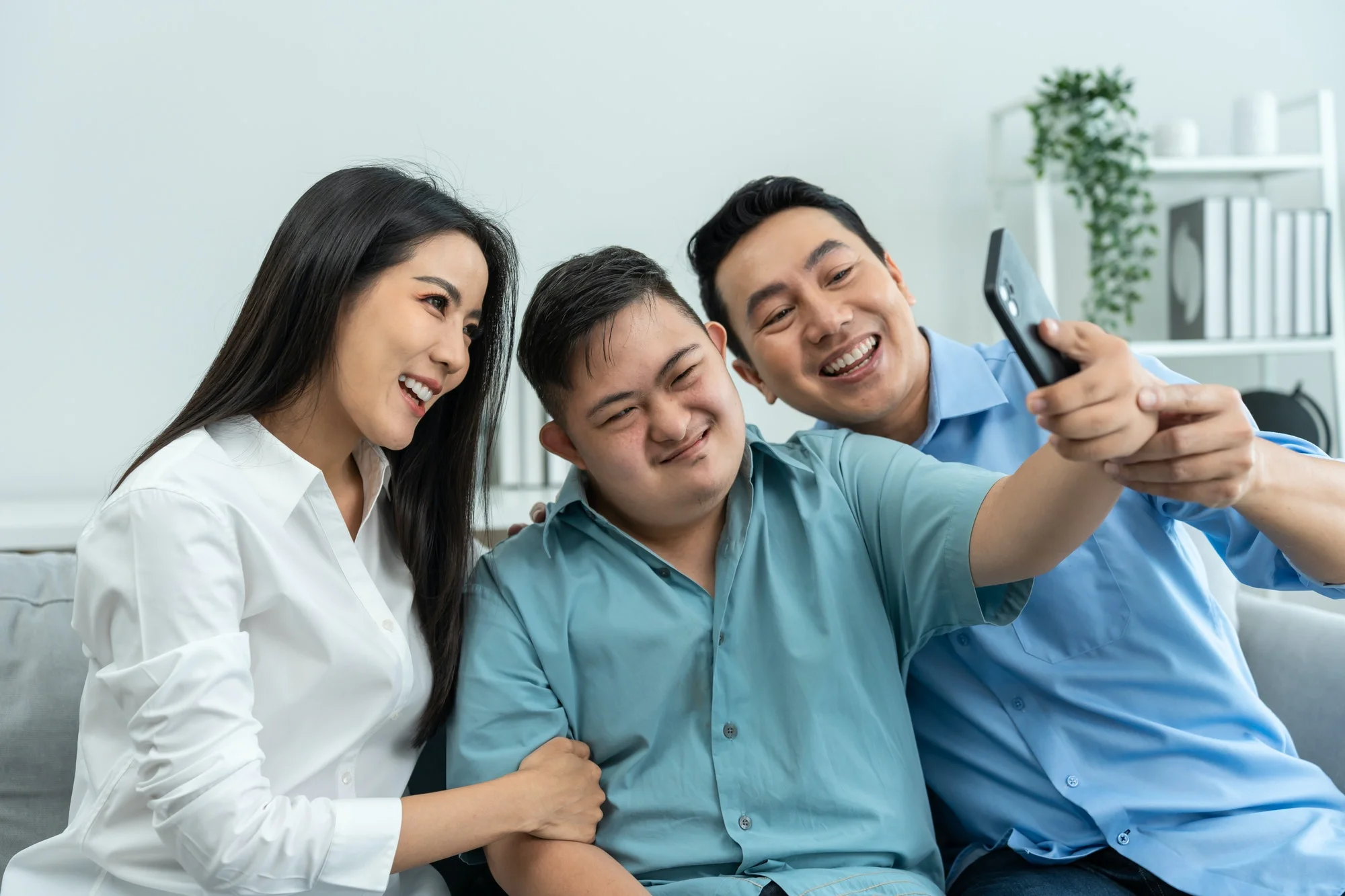 Asian parents and son with autism using phone take a selfies at home.