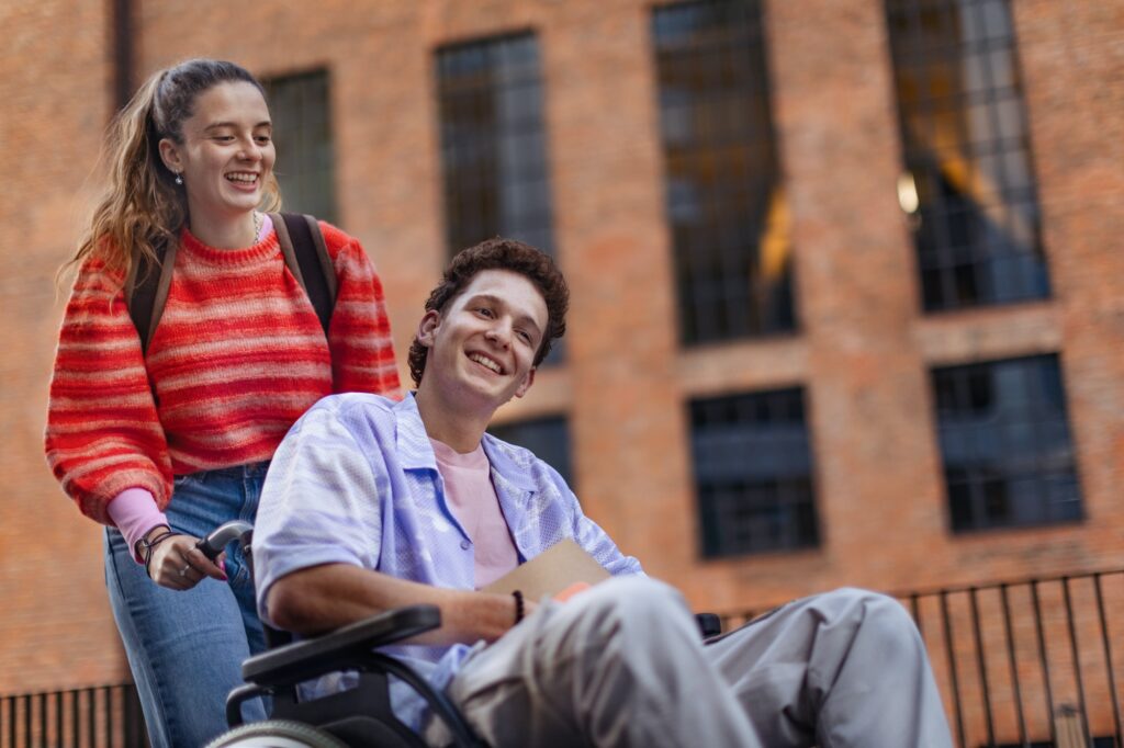 Handsome gen Z boy in wheelchair with friend in the city. Inclusion, equality, and diversity among